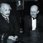 Два мужчины в классических костюмах за круглым столом в помещении, на фоне картина.