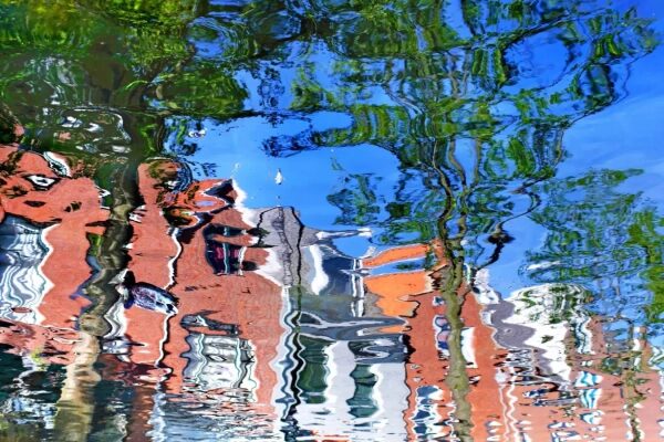 Отражение городских зданий и деревьев в волнах воды на фоне синего неба.