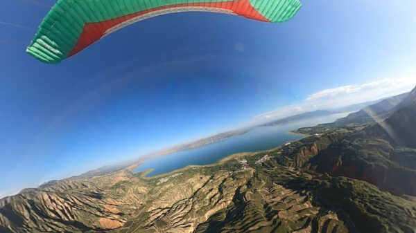 Параплан над живописным ландшафтом с озером и горами под голубым небом.