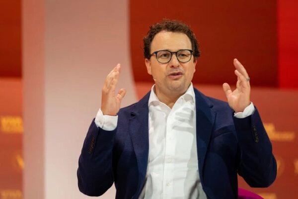 Мужчина в очках в костюме говорит на сцене, жесты руками. Конференция, оратор, выступление.