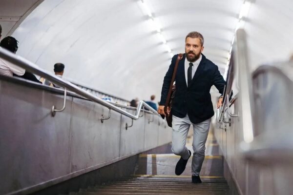Мужчина в костюме поднимается по лестнице в метро, держа портфель через плечо.