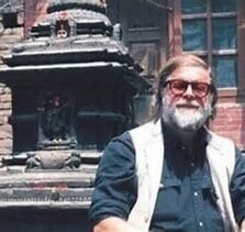 Мужчина с бородой и в очках на фоне архитектурного памятника.