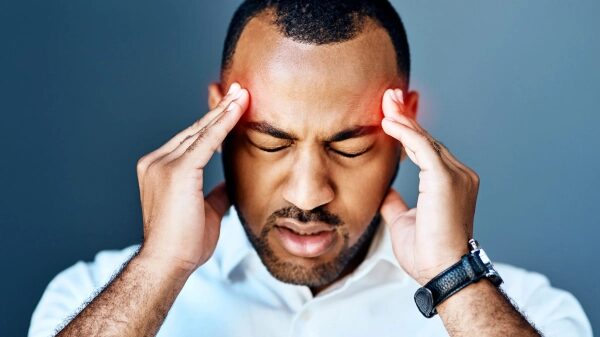 Мужчина держится за голову, страдает от головной боли или стресса, на сером фоне.