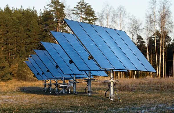Солнечные батареи на поле, окружённом лесом, ясная погода.