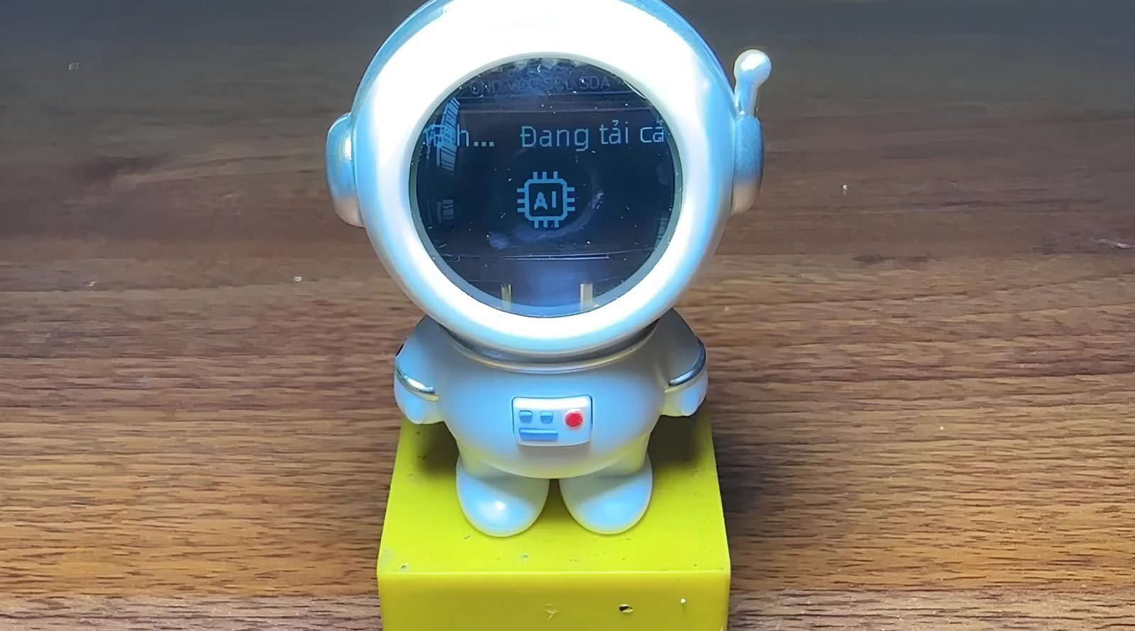 Астронавт с характером: ИИ-ассистент внутри фигурки 2 Фигурка астронавта с экраном, показывающим загрузку AI, стоит на деревянной поверхности.