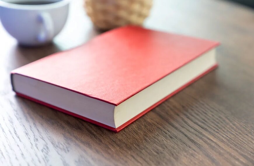 Красная книга на деревянном столе рядом с чашкой кофе.