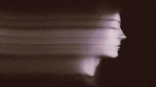 Размытый силуэт лица в движении на тёмном фоне, эффект размытия.