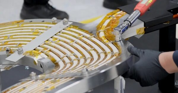 Работник в перчатках собирает электромагнитную установку с проводами и инструментами.