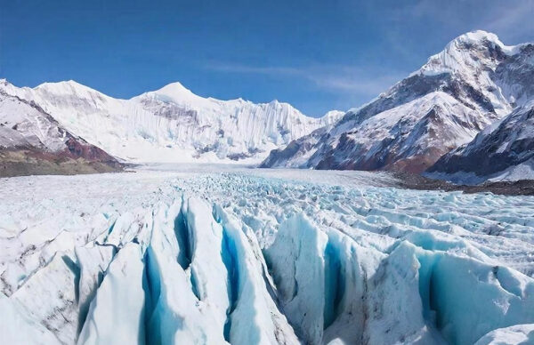 Горный ледник под ярким небом, окруженный снежными вершинами.