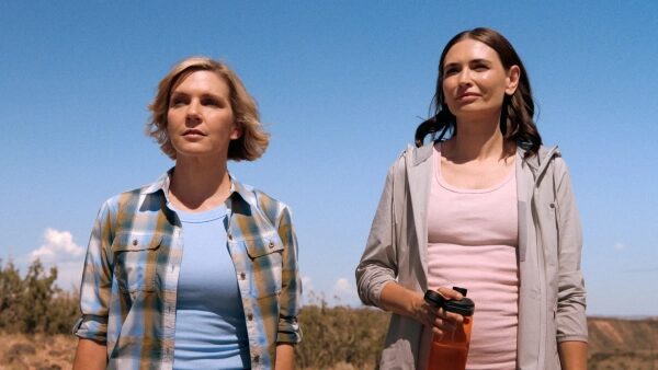 Две женщины на открытом воздухе в ясную погоду, одна держит бутылку.