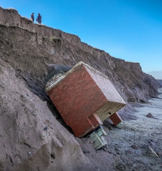 Обвал грунта: кирпичное здание скатывается по обрыву, люди наблюдают сверху.