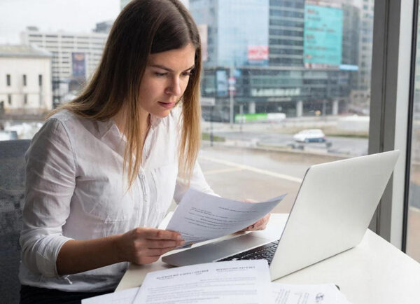 Женщина с ноутбуком изучает документы у окна в офисе.