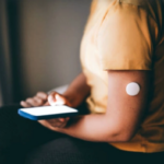 Человек с датчиком на руке использует смартфон, сахарный диабет, мониторинг глюкозы.