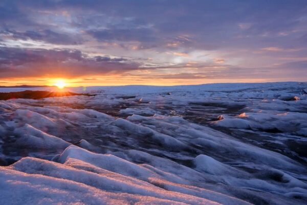Закат над снежной равниной, ледяные структуры на фоне теплого неба.