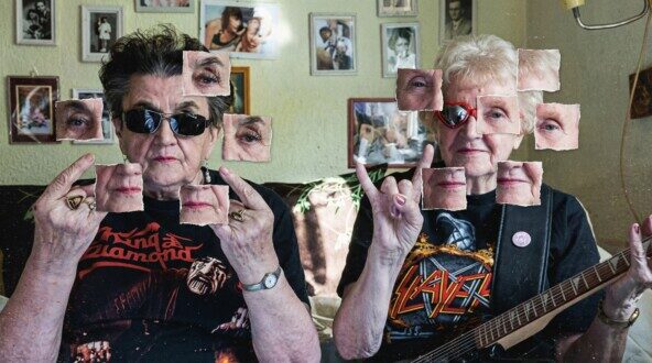 Два человека в футболках с рок-символикой показывают "козу" в домашней обстановке.