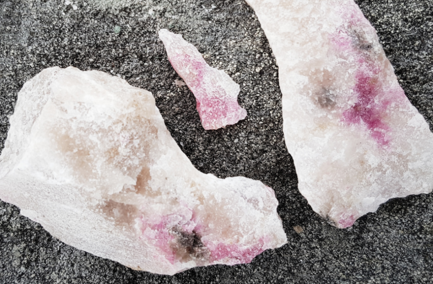 Кристаллы розового турмалина на серой поверхности, природные минеральные образцы.
