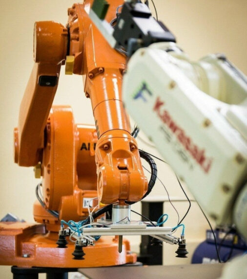 Промышленные роботы на заводе, крупный план оранжевого и белого манипуляторов.