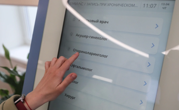 Пациент выбирает врача на медицинском терминале, касаясь экрана.