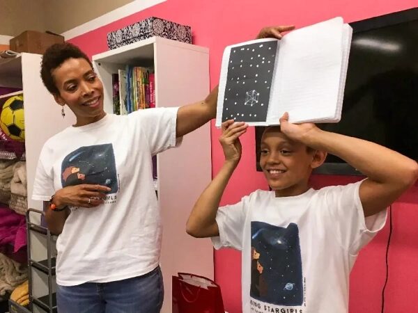 Шилдс стоит рядом с ребёнком, который держит над головой открытую тетрадь.