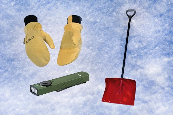 Зимние перчатки, лопата и фонарик на фоне снега.