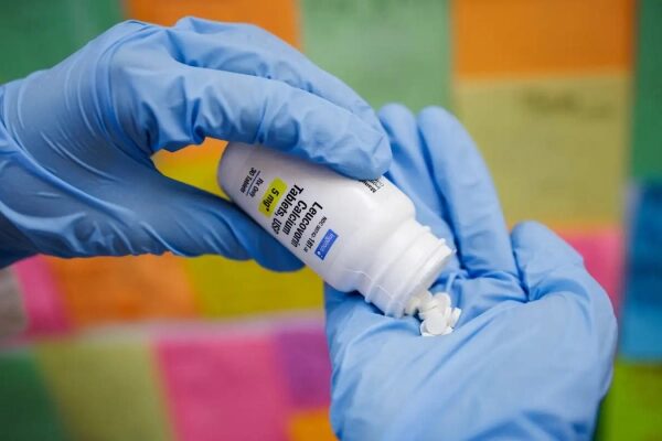 Перчатки на руках, таблетки из белой бутылки, на фоне цветные квадраты.