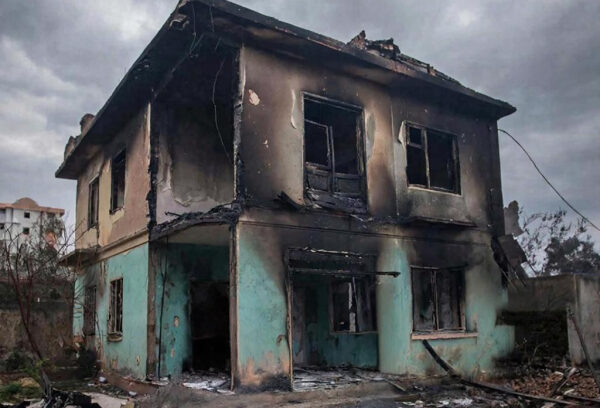 Сгоревший двухэтажный дом с обгоревшими стенами и окнами после пожара.