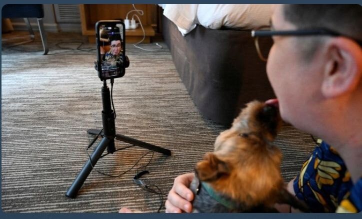 Человек с собакой перед телефоном на штативе в комнате.