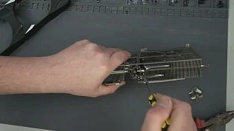 Сборка и ремонт видеокарты на сером столе, видны руки и отвертка.
