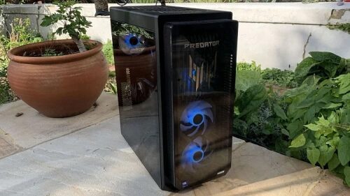 Игровой компьютер Predator с подсветкой на открытой террасе рядом с зелеными растениями.