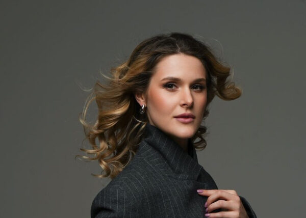 Женщина в сером костюме с распущенными волосами на сером фоне.