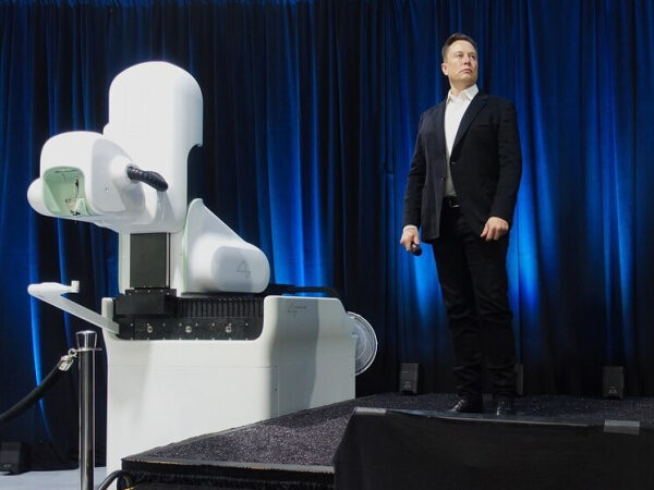 Человек в костюме стоит рядом с роботом на сцене с синим фоном.
