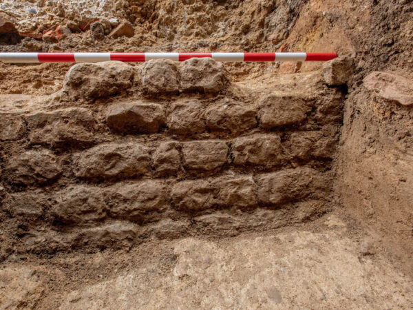 Археологическая раскопка: древняя каменная кладка с измерительной рейкой.