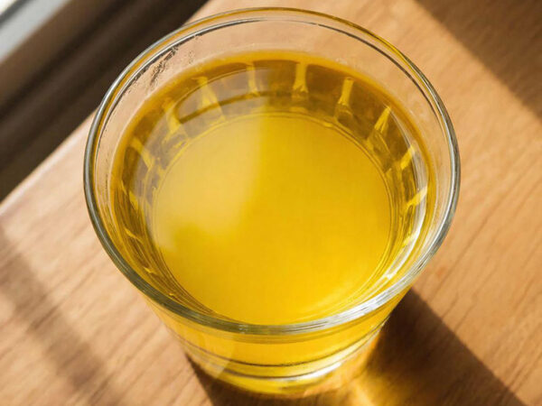 Стакан с желтой жидкостью на деревянном столе, солнечный свет.
