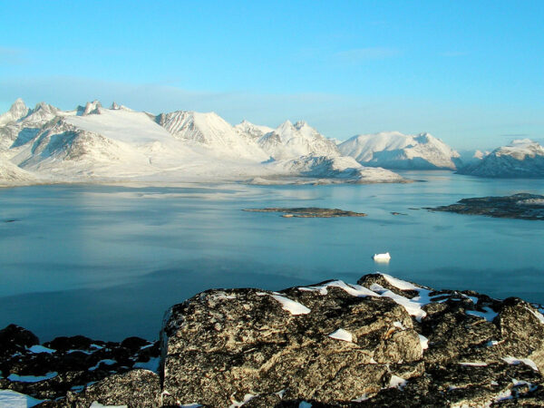 Заснеженные горы у берегов фьорда в Гренландии, спокойная вода, ясное небо.