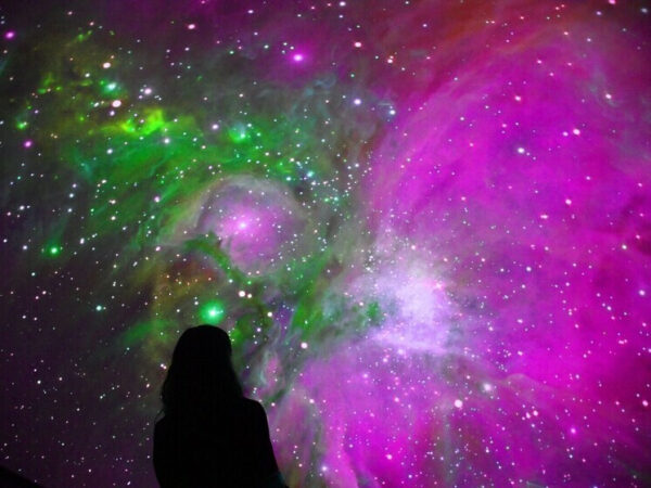 Человек смотрит на яркую фиолетово-зеленую туманность в космосе.