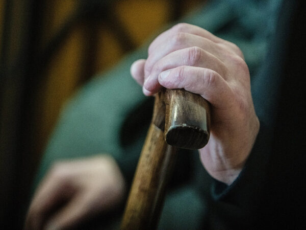 Рука на деревянной трости вблизи, человек в темной одежде.