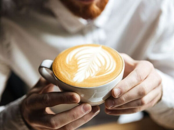 Капучино с рисунком на молочной пенке в белой чашке в руках мужчины.
