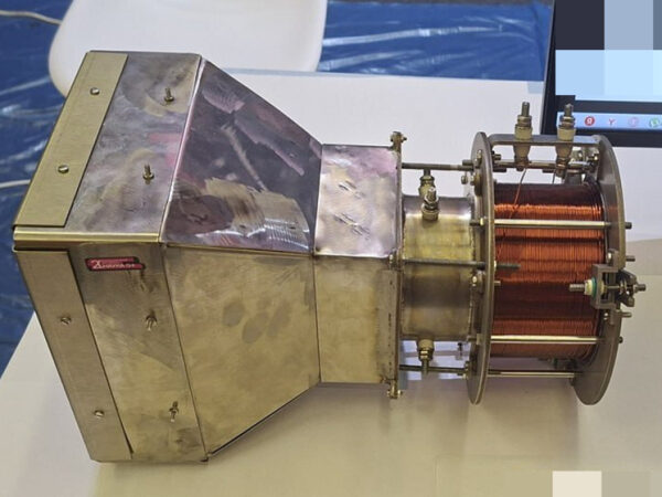 Металлический прибор с медной катушкой на столе, вид сбоку.