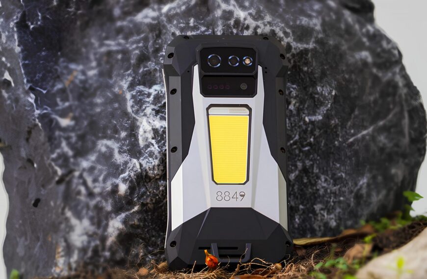 Защищённый смартфон с тремя камерами и прочным корпусом на фоне камней.