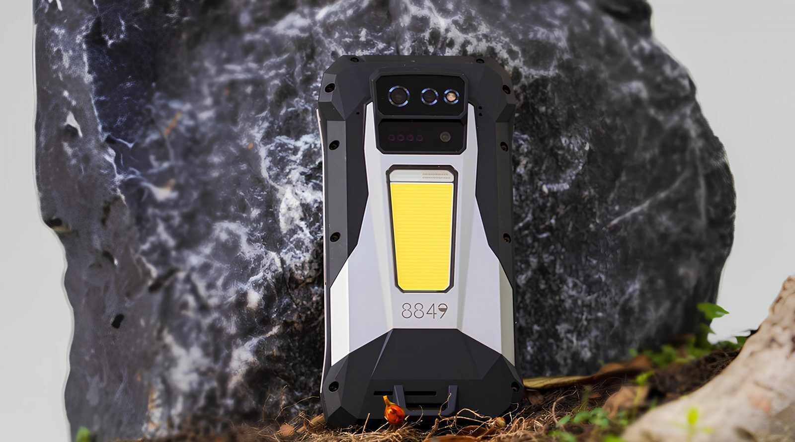 Защищённый смартфон с тремя камерами и прочным корпусом на фоне камней.