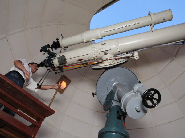 Человек управляет большим телескопом в обсерватории под куполом.