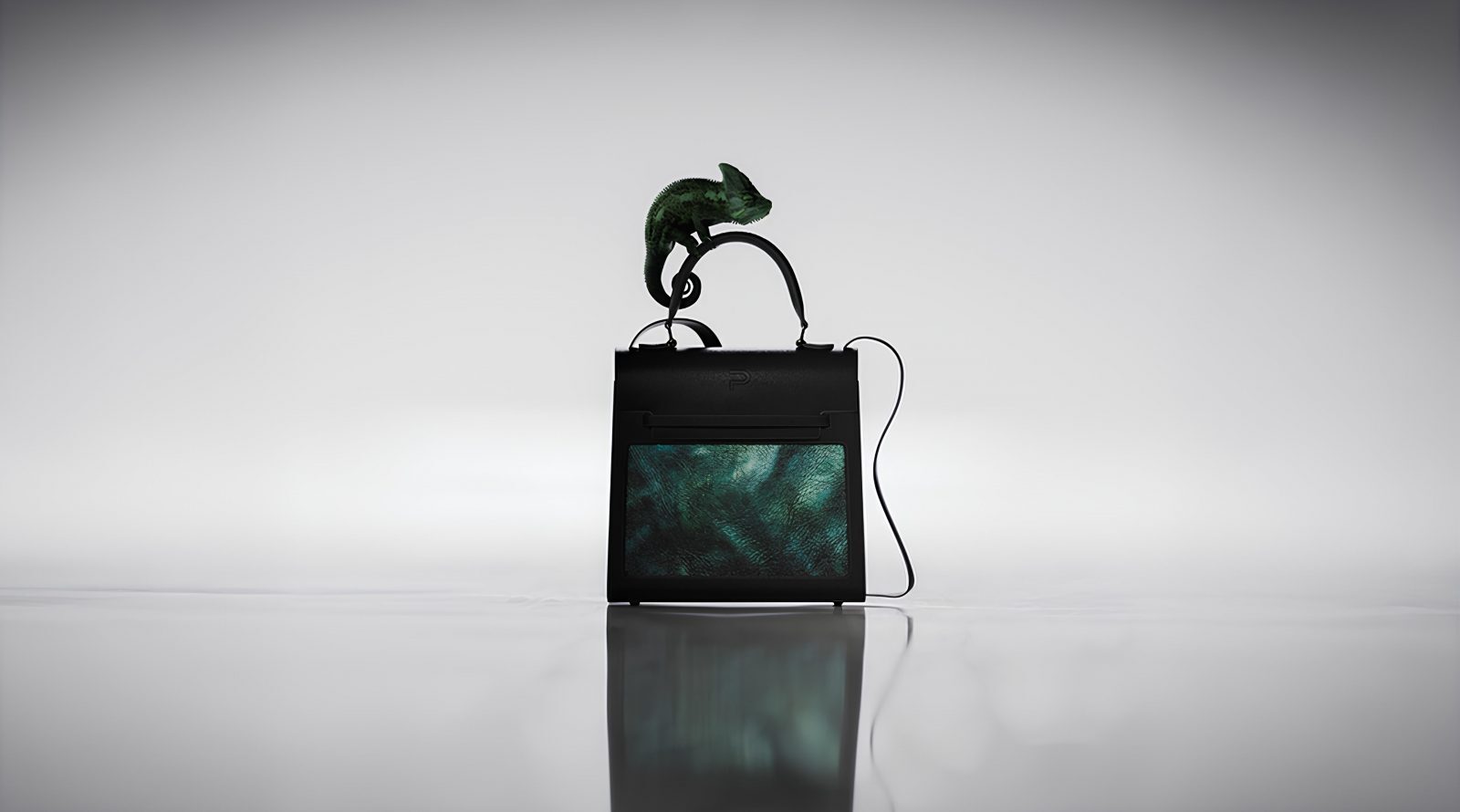 Сумка Infinity на стыке моды и технологий 1 Черная сумка с зеленым хамелеоном сверху, серый фон.