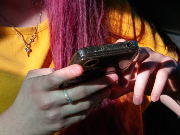 Девушка с розовыми волосами в жёлтой футболке держит смартфон в руках.