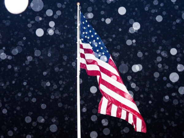 Флаг США развевается ночью на фоне снежинок.