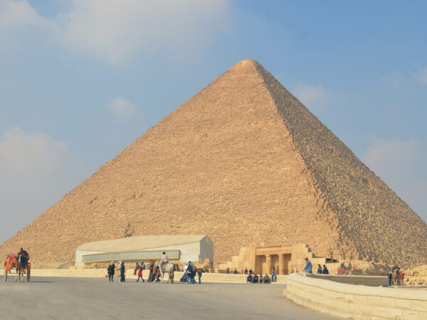 Пирамида Хеопса в Гизе, Египет, туристы гуляют у подножия, ясное небо.