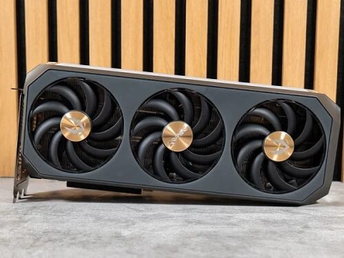 Видеокарта с тремя вентиляторами на фоне деревянной панели.