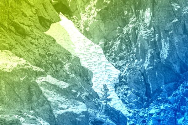 Скалы с разноцветной наслоенной обработкой и снежным участком в ущелье.