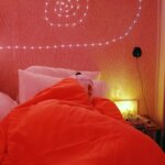 Человек спит в кровати с оранжевым одеялом и светодиодной подсветкой на стене.