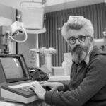 Человек за ретро-компьютером в лаборатории, черно-белое фото.