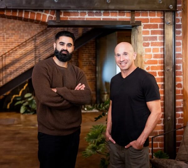 Два мужчины в современном интерьере с кирпичными стенами и растениями.